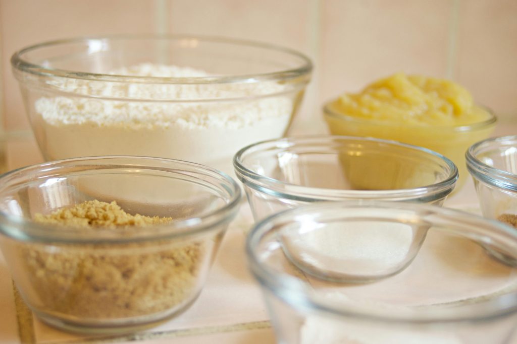 Close-up of baking ingredients in glass bowls, showcasing flour, sugar, and more for food preparation.