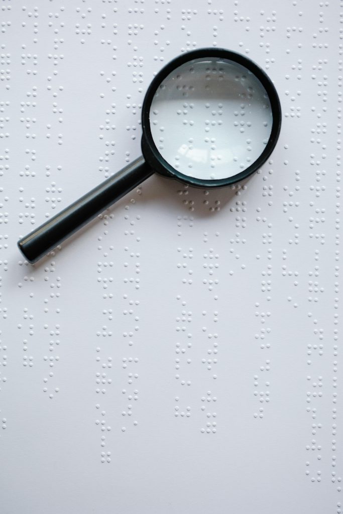 Close-up of a magnifying glass highlighting Braille text on white paper.