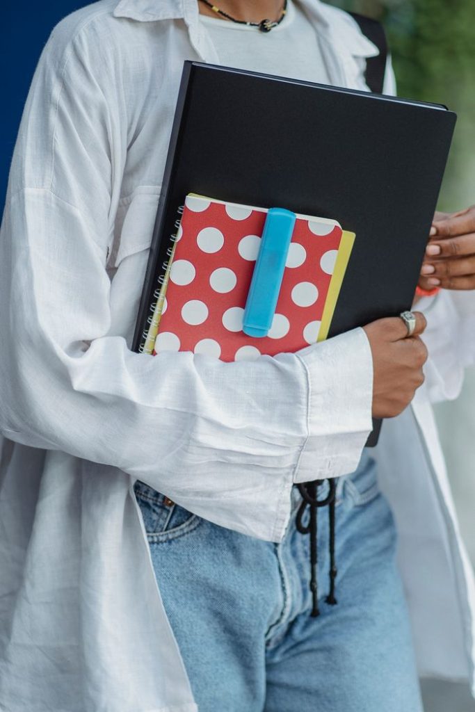 Crop anonymous ethnic female in casual wear with collection of exercise books in daytime