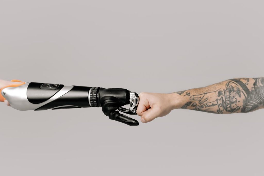 Close-up of a tattooed arm fist bumping with a robotic prosthetic arm in studio setting.